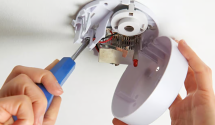 A person conducting a fire alarm maintenance in Perth using a screwdriver
