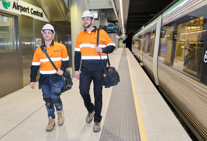 Two workers in safety gear walking near a train, heading to their next project site for fire suppression system installation
