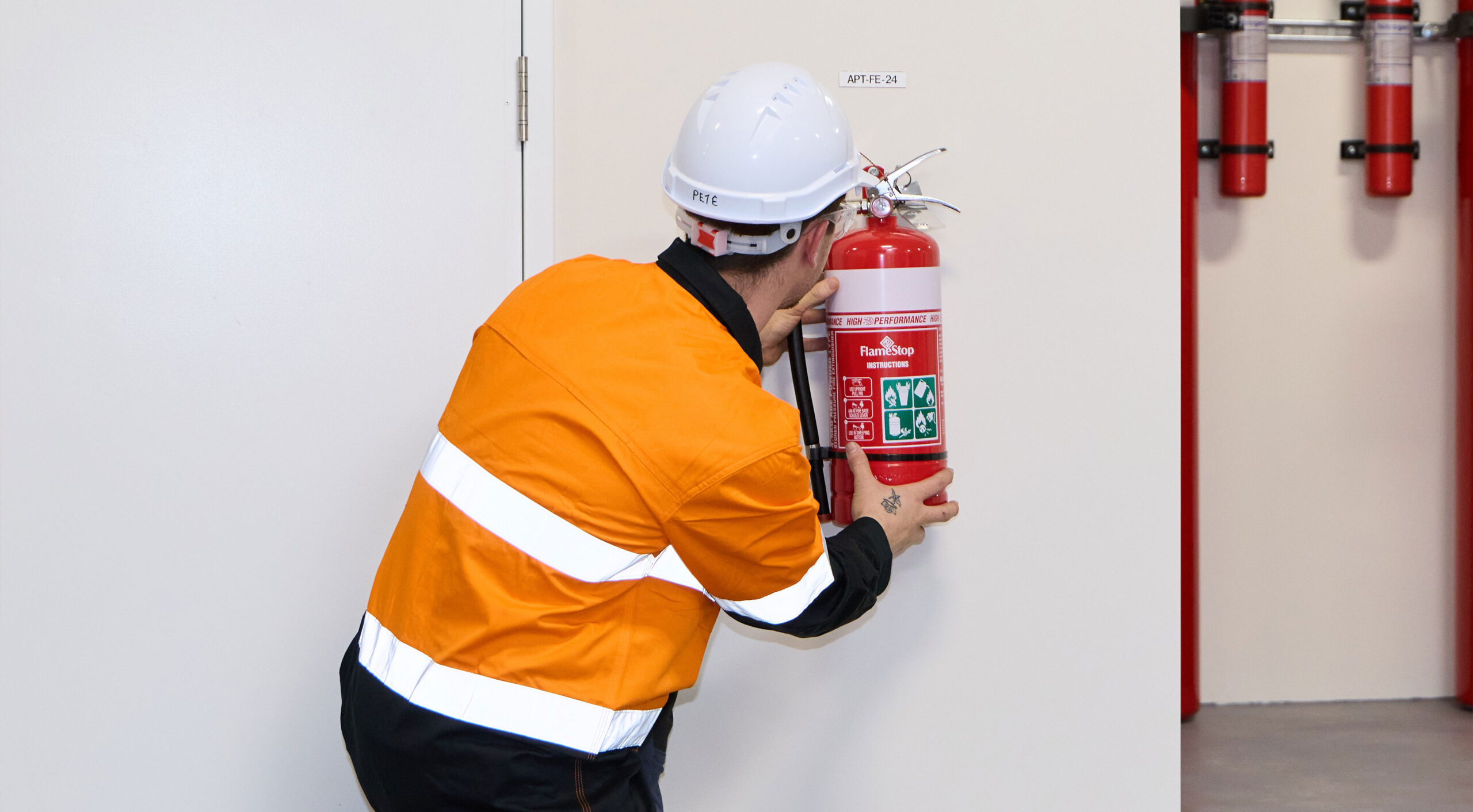 A man in an orange vest and hard hat holds a fire extinguisher, representing Fire Protection Services WA maintenance and compliance